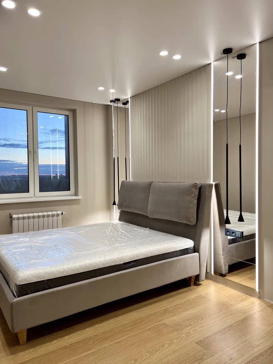 Nowoczesna sypialnia z szarym łóżkiem, lustrami z oświetleniem LED po bokach i gładkim białym sufitem z punktowymi lampami