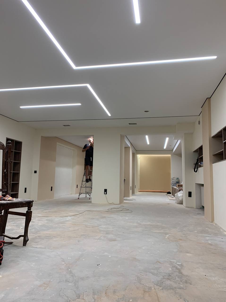 Montaż liniowego oświetlenia LED na suficie podwieszanym w przestronnym pomieszczeniu w trakcie remontu, widoczny pracownik na drabinie.