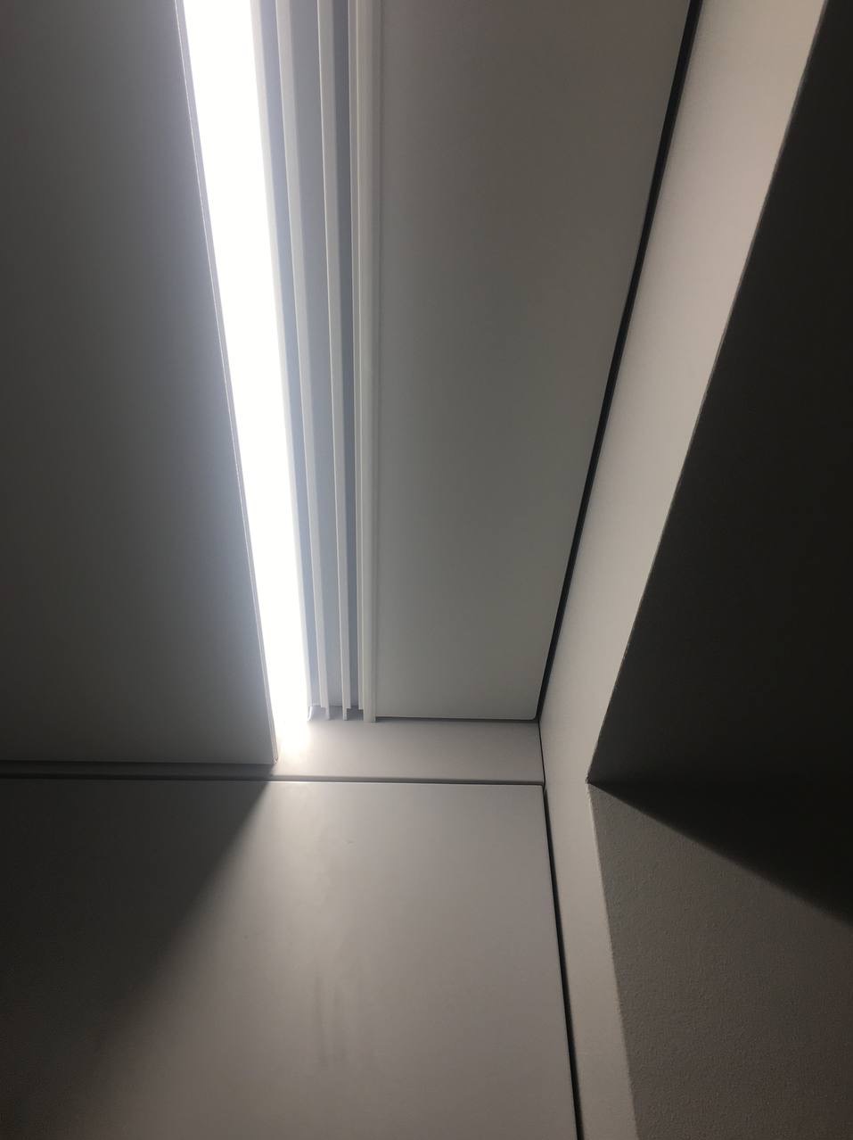 Fragment białego sufitu z oświetleniem LED, widoczne łączenie paneli i kąt ściany z efektem cienia.
