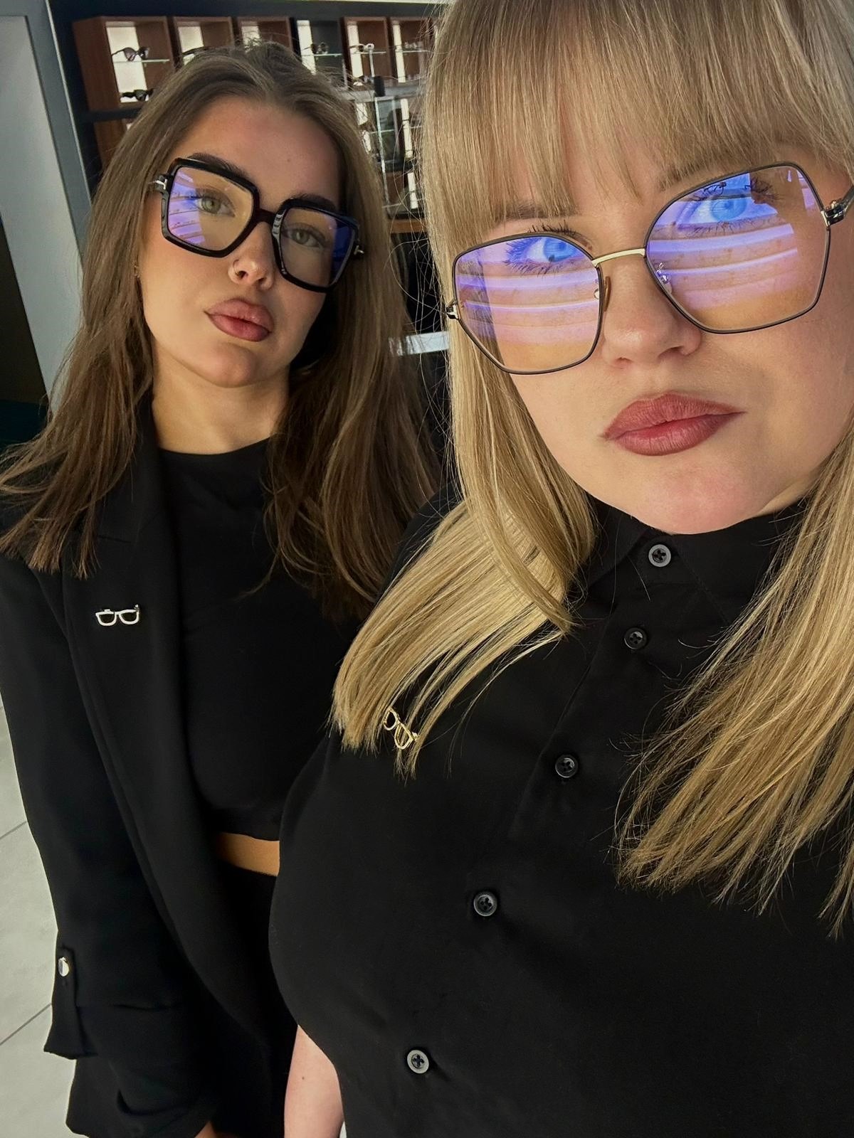 Dwie kobiety w Szczecinie prezentują modne okulary korekcyjne o różnych kształtach oprawek, z widocznymi odbiciami w szkłach i dopasowanymi przypinkami w kształcie okularów.