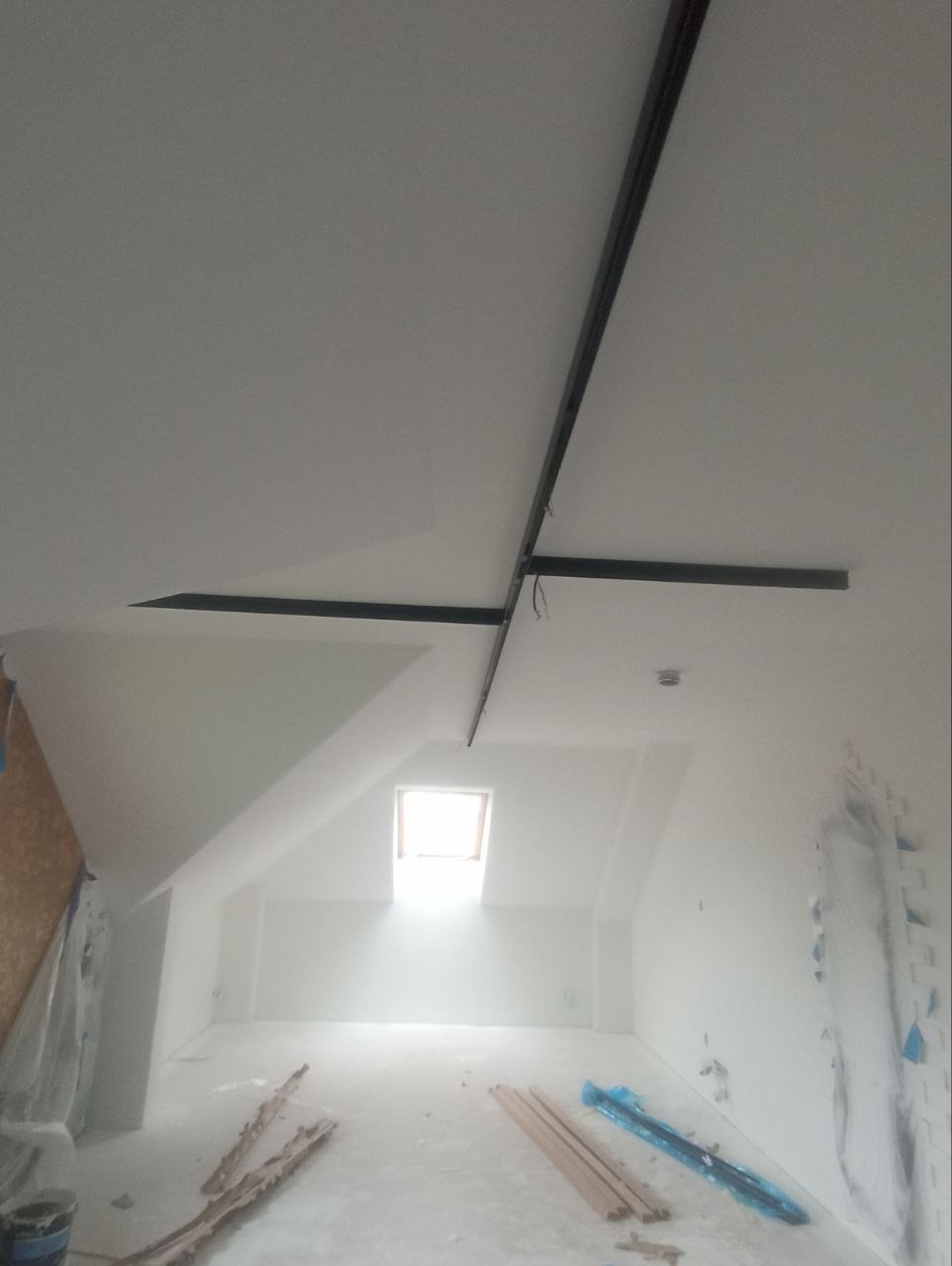 Stelaż pod instalację grzewczą na poddaszu z oknem dachowym, widok z dołu. Elementy instalacji przymocowane do sufitu, podłoga przygotowana do dalszych prac.