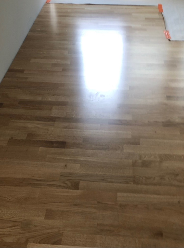 Świeżo ułożone, lakierowane panele podłogowe z widocznymi pomarańczowymi elementami zabezpieczającymi przy ścianie.