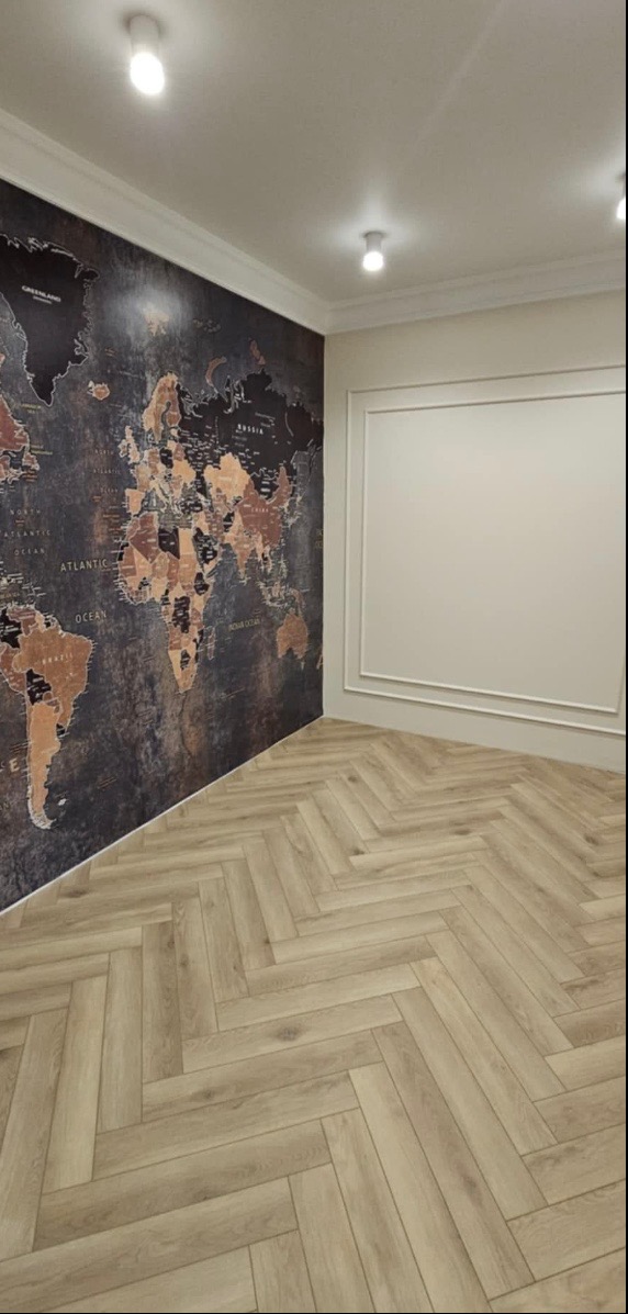 Pokój z ułożoną podłogą z paneli w jodełkę, ściana z tapetą w mapę świata i białą ścianą z dekoracyjną ramą.