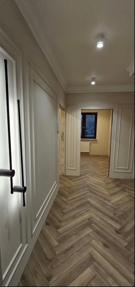 Korytarz po remoncie z parkietem ułożonym w jodełkę, oświetleniem punktowym i ozdobnymi listwami przypodłogowymi.