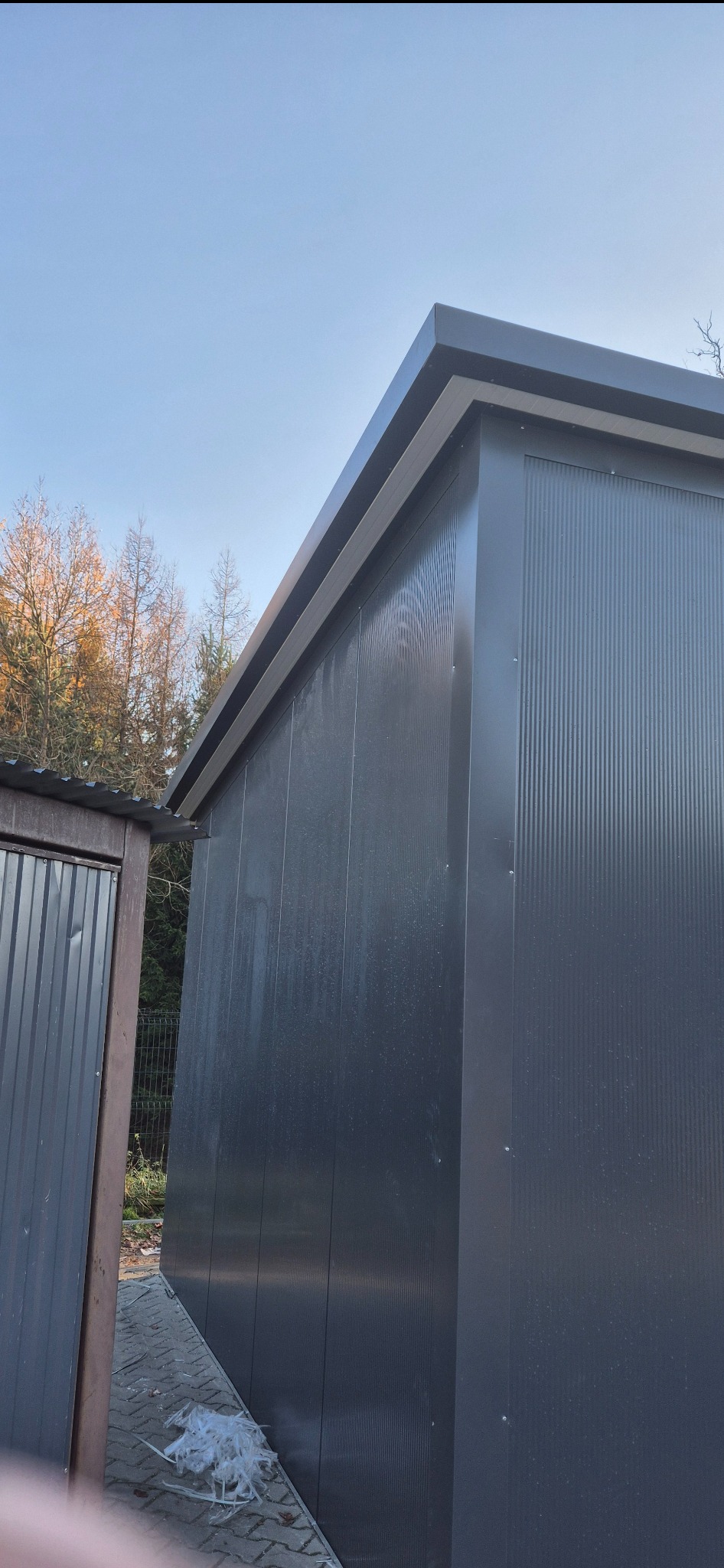 Nowoczesna hala z płyt warstwowych w Lubieniu, widok z zewnątrz. Szara elewacja z wyraźnymi pionowymi panelami, minimalistyczny design i czyste linie architektoniczne.