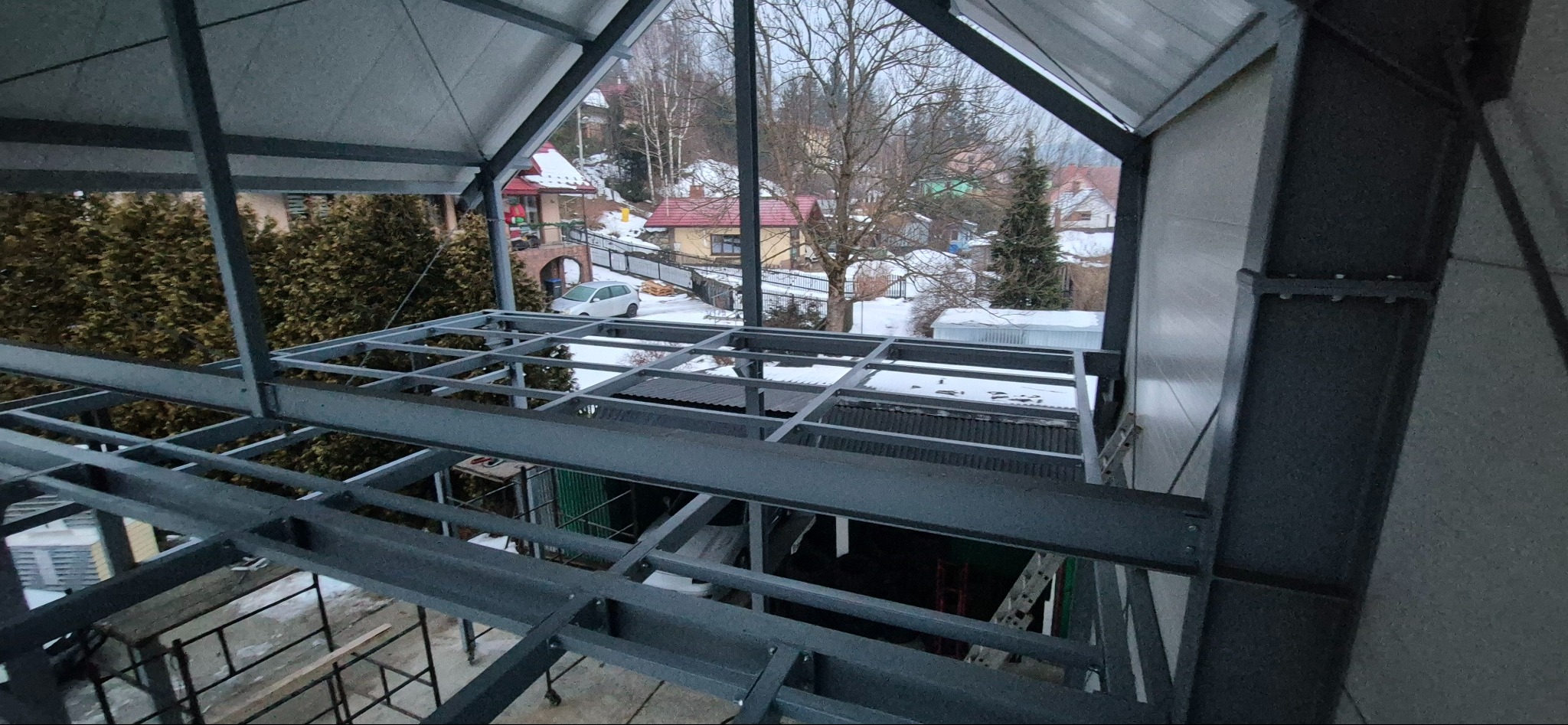 Konstrukcja stalowa hali w trakcie budowy, widok z góry na szkielet z profili, w tle zabudowa jednorodzinna w zimowej scenerii.