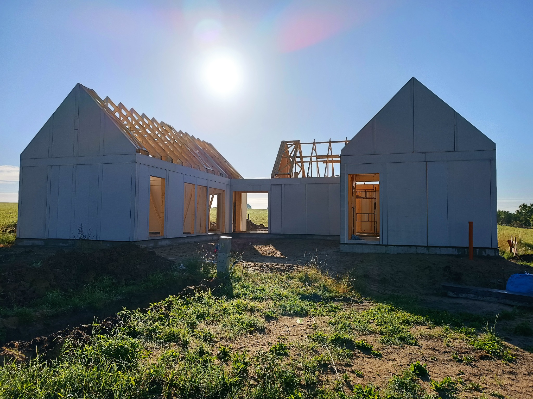 Surowy stan domu modułowego z widoczną więźbą dachową w słoneczny dzień, na tle zielonego pola.