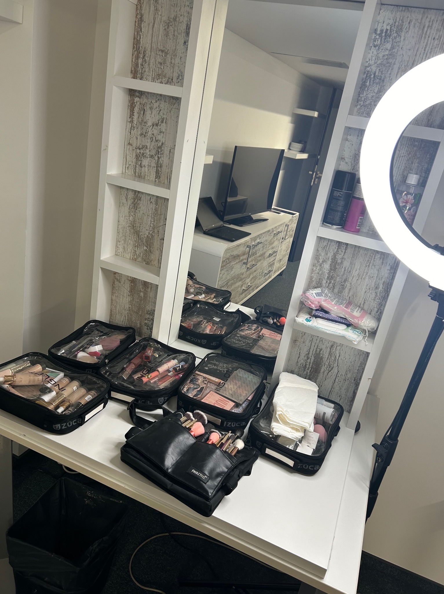 Stanowisko do makijażu w Warszawie: torby z kosmetykami ZUCA, pędzle MyKitCo, lampa pierścieniowa i lustro z półkami.