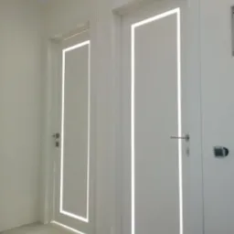 Dwa białe skrzydła drzwiowe z podświetleniem LED w kształcie prostokąta, minimalistyczny design, widoczny fragment szarej podłogi i białe ściany.