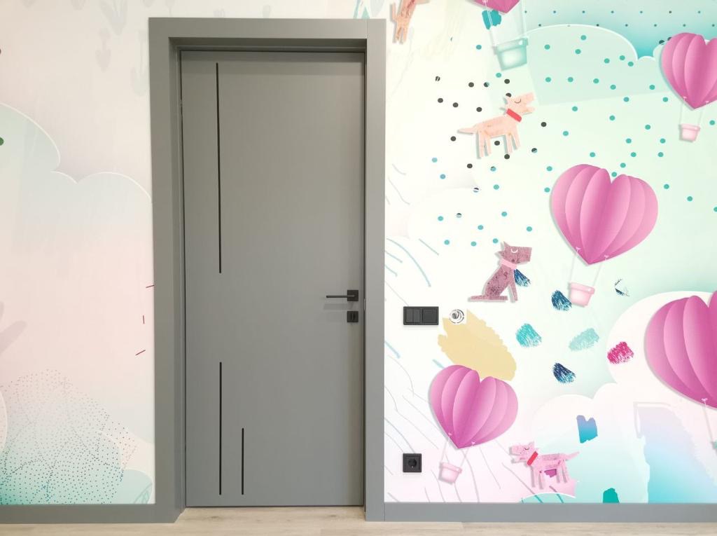 Szare skrzydło drzwiowe z trzema pionowymi, czarnymi frezami, zamontowane w szarej ościeżnicy, na tle ściany z dziecięcą tapetą w balony i pieski.
