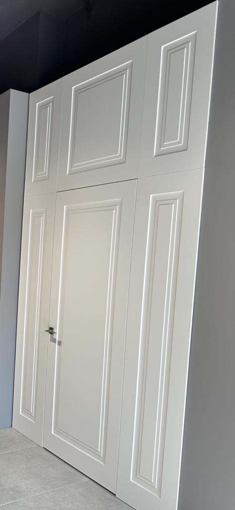 Białe drzwi wewnętrzne z dekoracyjnymi frezami w Warszawie, zamontowane w nowoczesnym wnętrzu z szarą ścianą i podłogą z płytek.