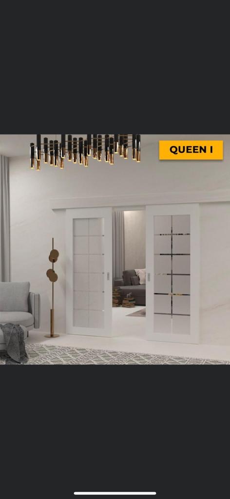 Nowoczesne, dwuskrzydłowe drzwi przesuwne z białymi ramami i matowym szkłem w kwadraty, widoczne w jasnym wnętrzu z designerską lampą i elementami dekoracyjnymi.