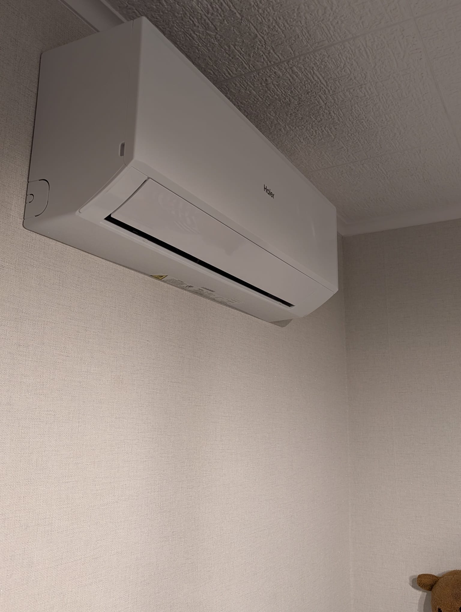 Biała klimatyzacja Haier na ścianie z tapetą w Sztumie. Widoczny fragment sufitu z fakturą. Minimalistyczny design, świeżo zamontowane urządzenie.