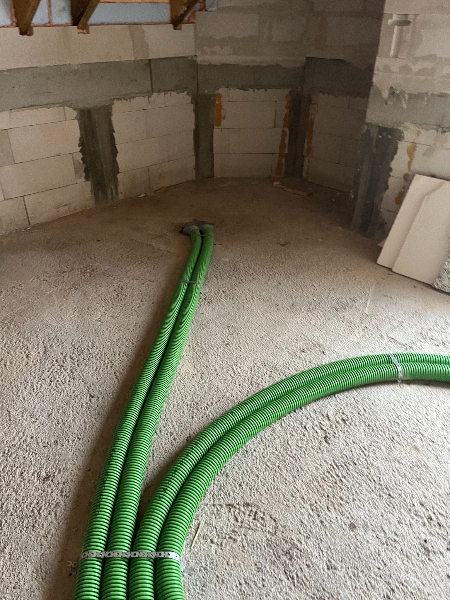 Zielone rury wentylacyjne ułożone na surowym podłożu w budynku w trakcie budowy w Sztumie. Widoczne ściany z betonu komórkowego.