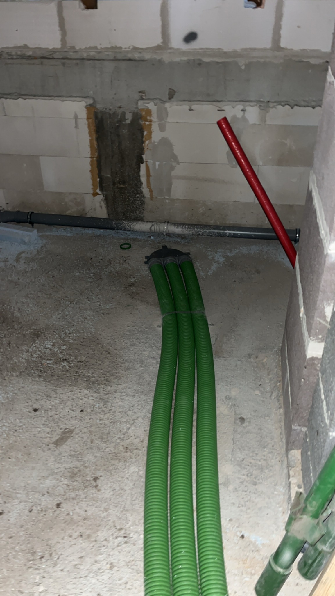 Surowy stan: zielone rury wentylacyjne w betonowej wnęce, widoczne szare rury i czerwony element instalacji. Ściany z pustaków.