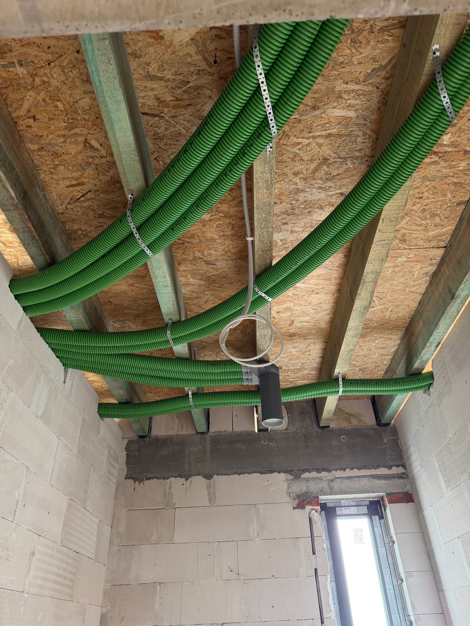 Zielone rury wentylacyjne zamontowane pod stropem z płyt OSB, widoczne elementy mocujące. Instalacja w trakcie realizacji w Sztumie.