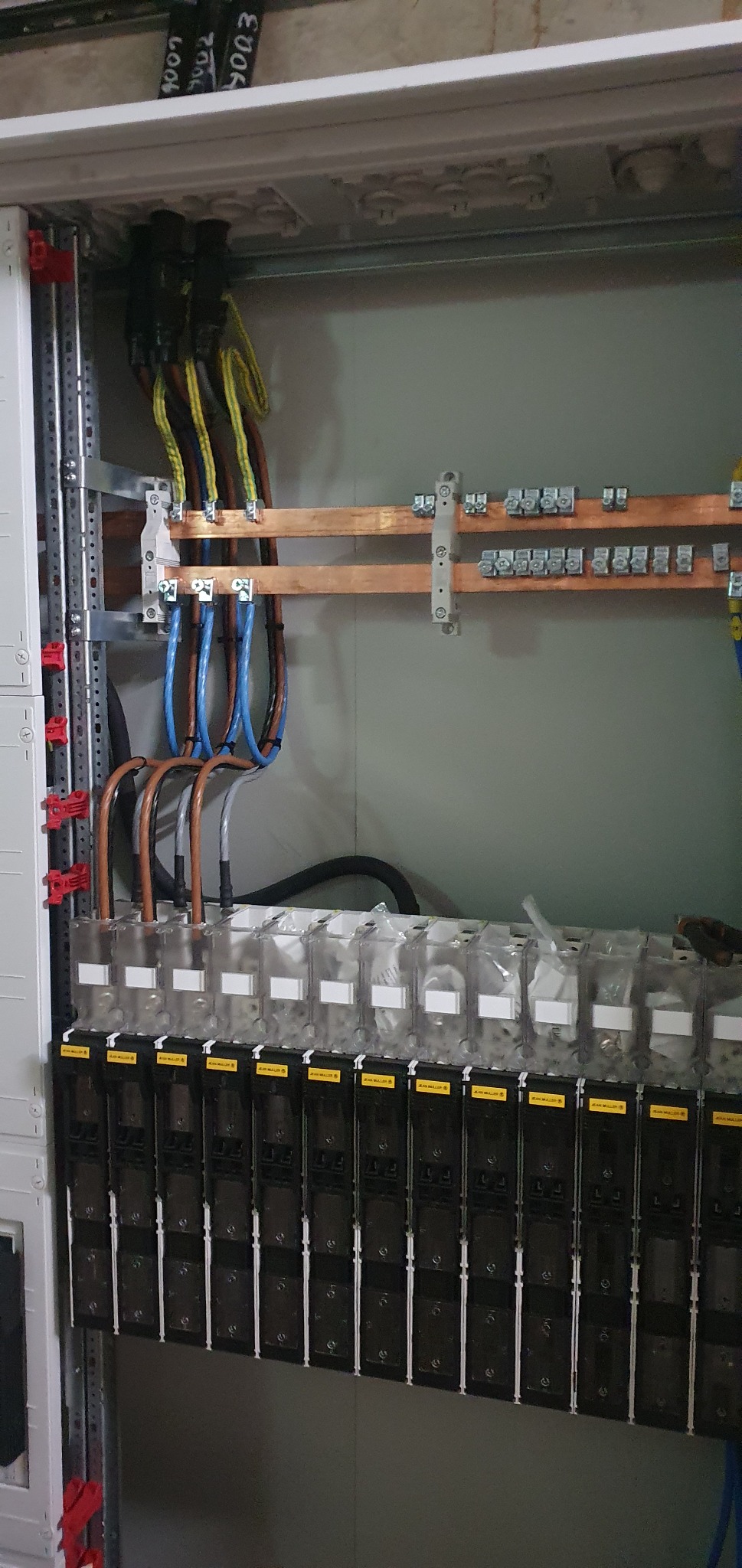 Rozdzielnia elektryczna w trakcie montażu, widoczne kable o różnych kolorach podłączone do szyny miedzianej i zabezpieczeń modułowych,  etykiety na przewodach z numerami 9002 i 9003.