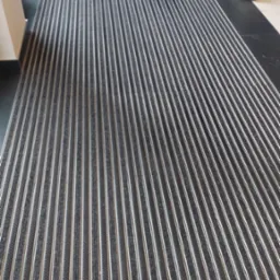 Szara wycieraczka systemowa z aluminiowymi listwami przed schodami wejściowymi do budynku.