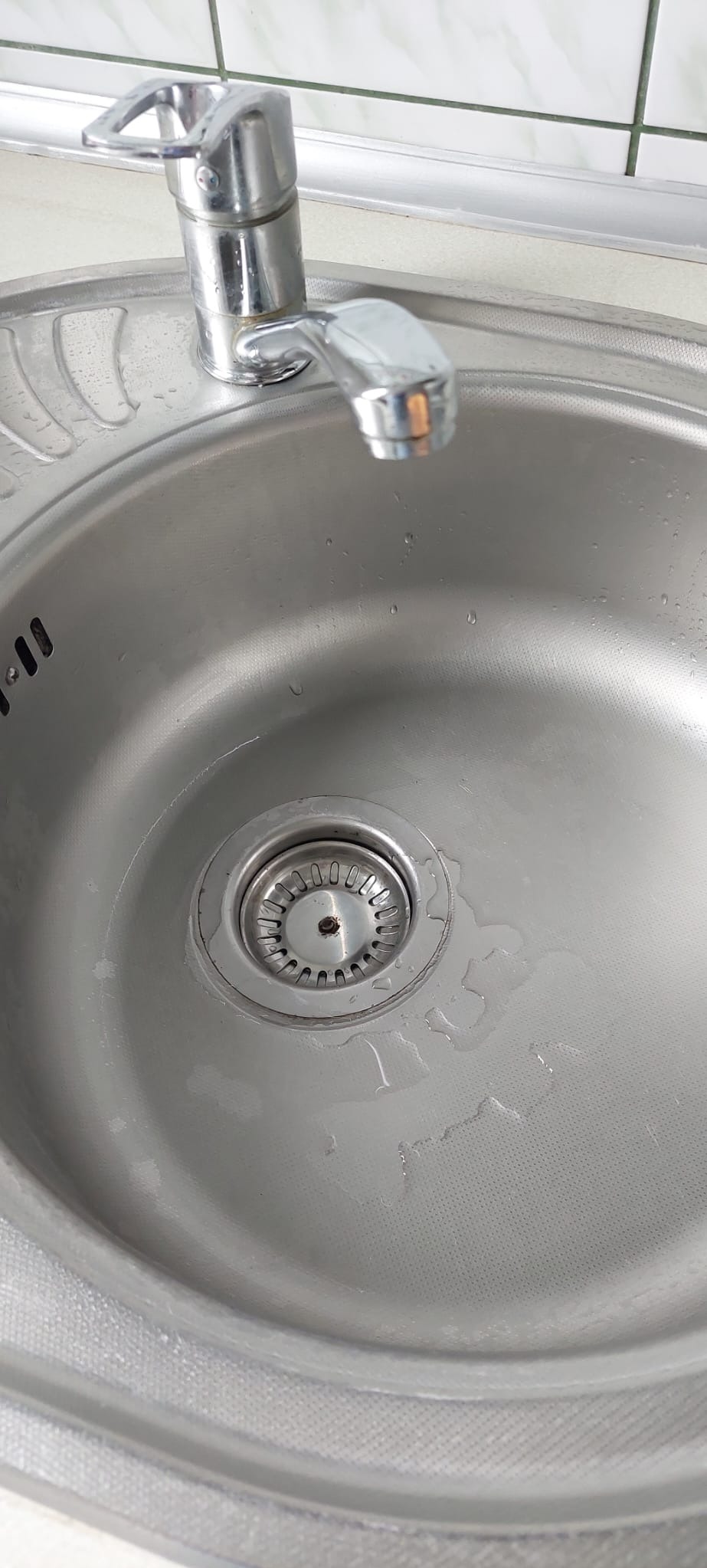 Błyszczący, stalowy zlew z chromowaną baterią i drobnymi kroplami wody, ukazujący detale faktury materiału i odpływu.