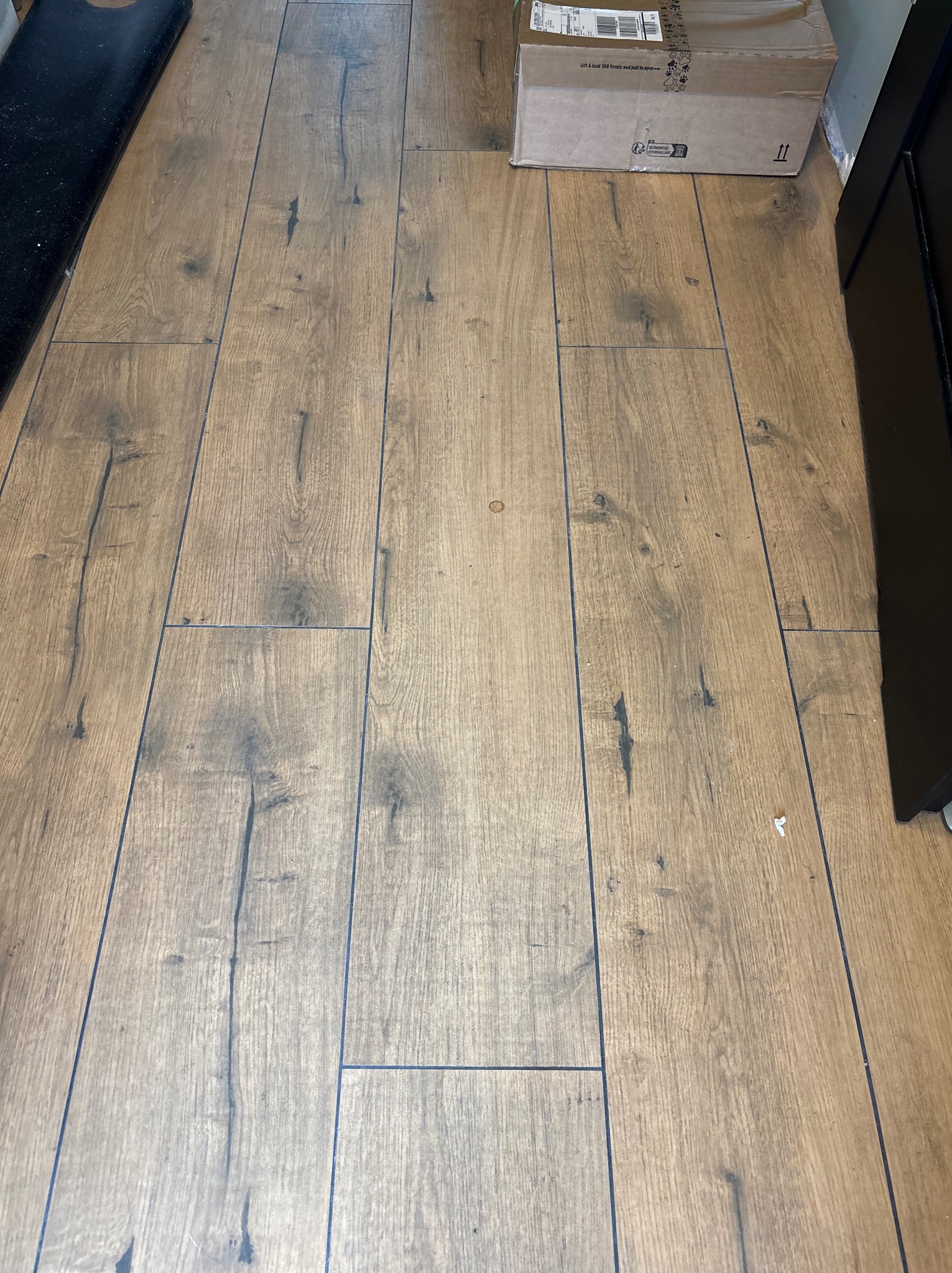 Ułożona podłoga z paneli imitujących drewno z widoczną strukturą i słojami, przy ścianie stoi karton.