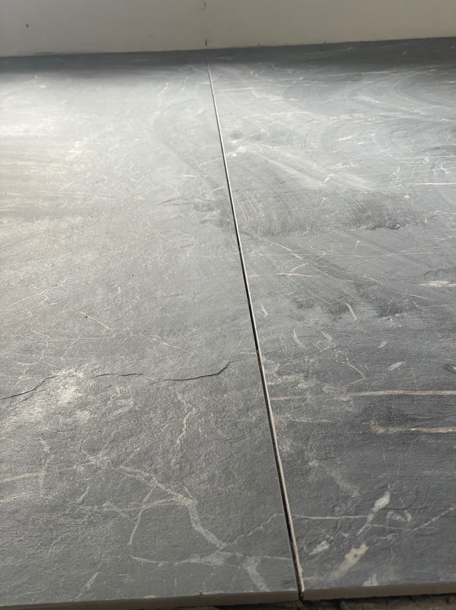 Położone płytki podłogowe imitujące kamień, widoczne fugi, szara kolorystyka, minimalizm.