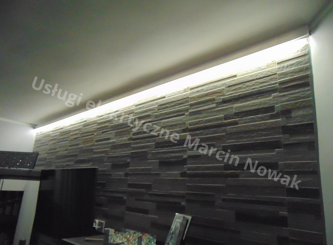 Światło LED zamontowane pod sufitem, oświetlające dekoracyjną ścianę z kamienia w salonie.