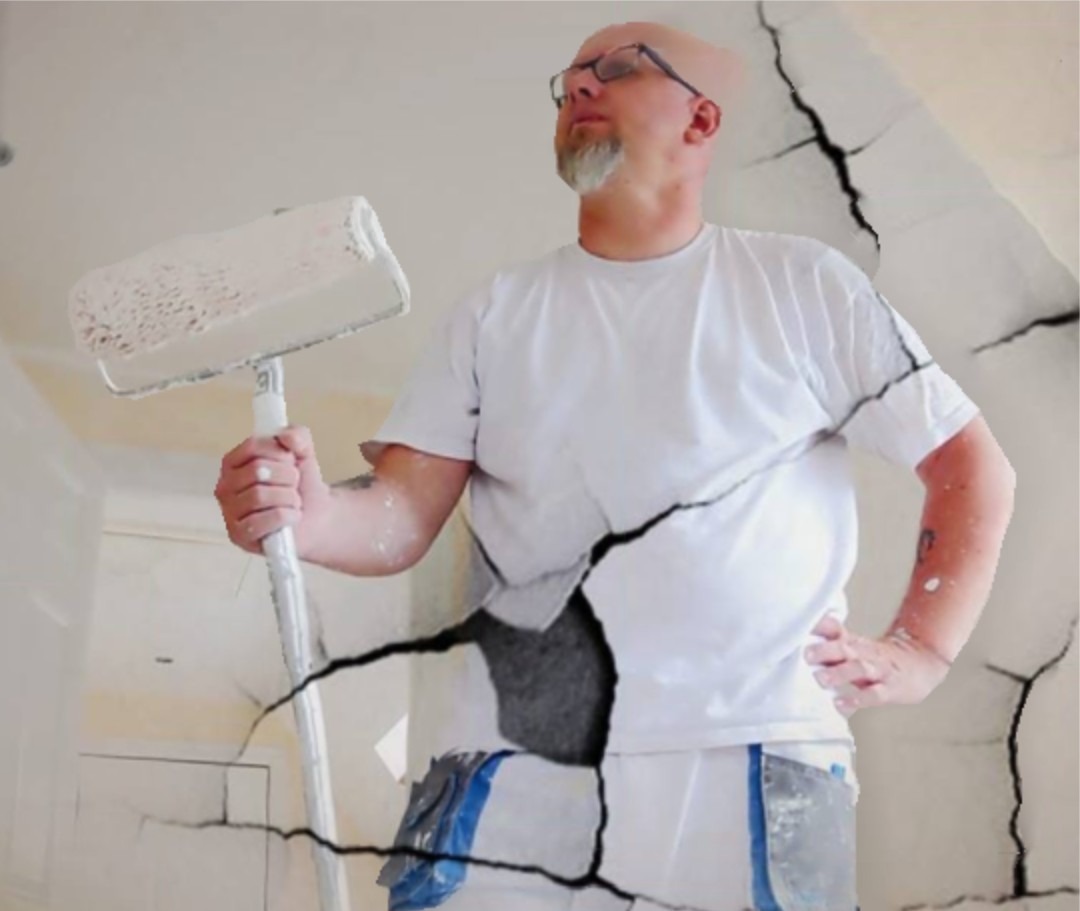 Mężczyzna z wałkiem do malowania, ubrudzony farbą, stoi na tle ściany z pęknięciami, spoglądając w górę.