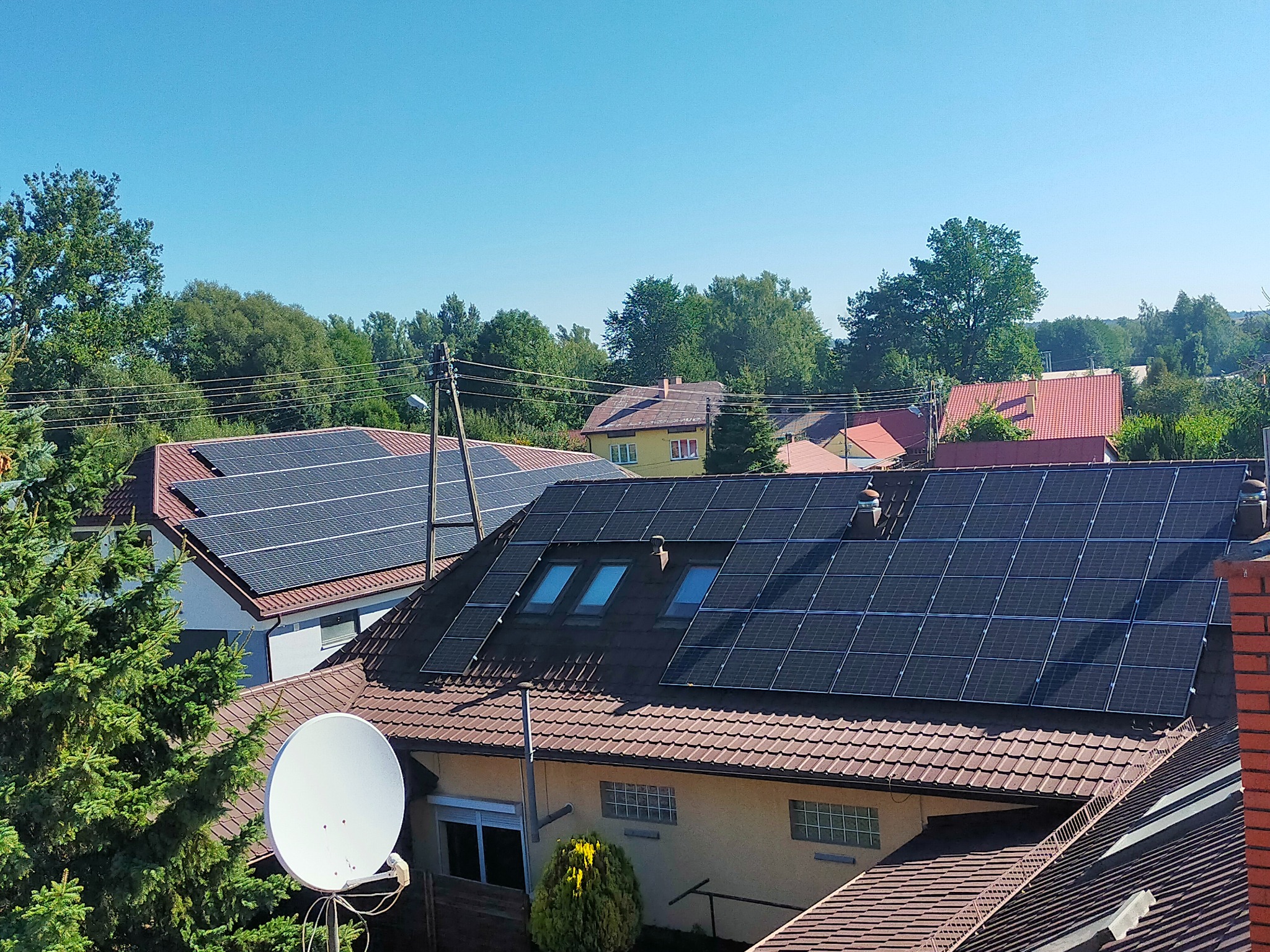 Panele słoneczne na dachach domów jednorodzinnych w słoneczny dzień, widok z góry, antena satelitarna w kadrze.