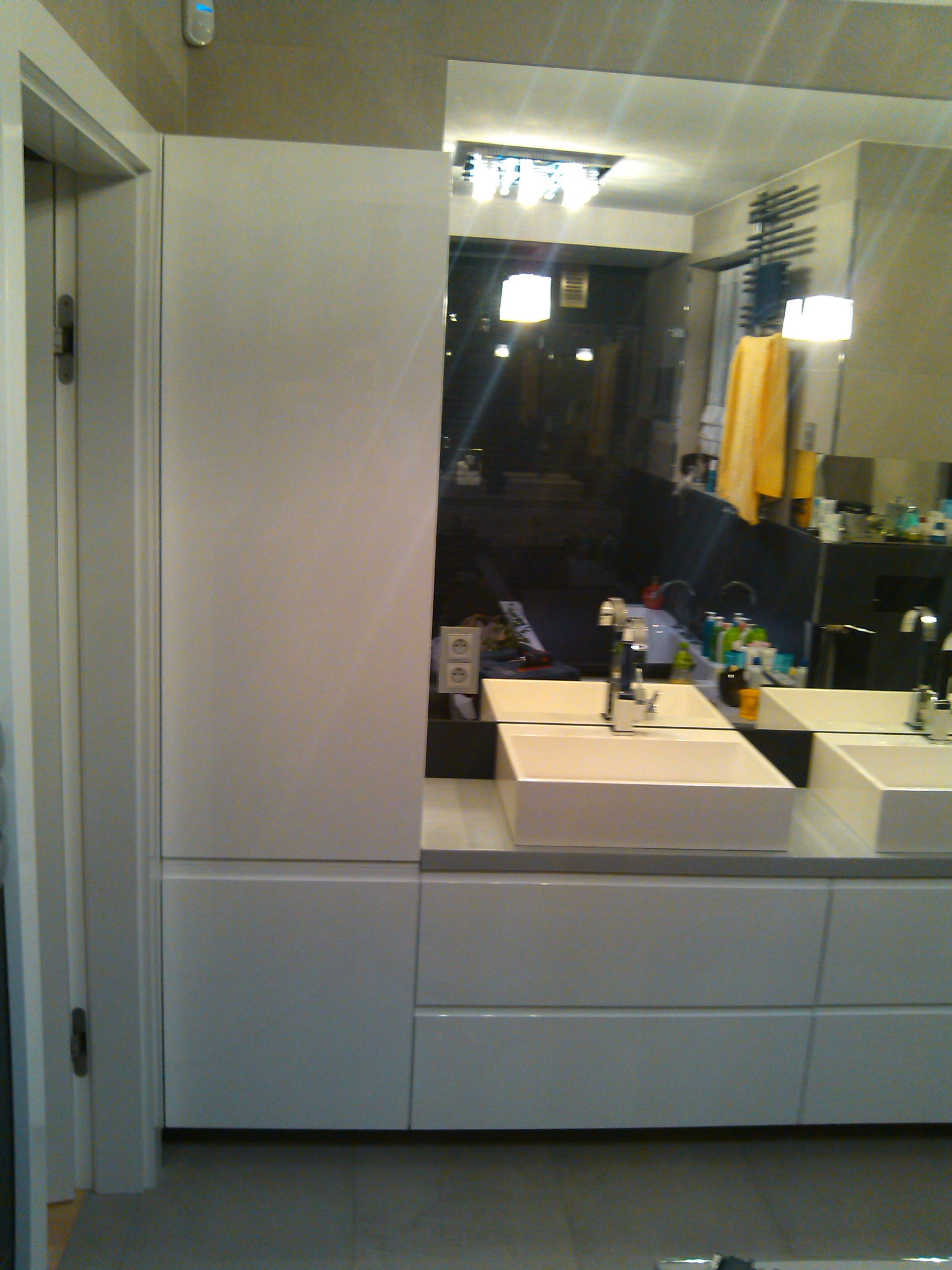 Nowoczesna łazienka z dwiema prostokątnymi umywalkami nablatowymi, dużym lustrem i białymi szafkami, widoczne gniazdko elektryczne na ścianie.