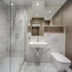 KRAWCZYK - Nowoczesna łazienka z kabiną prysznicową typu walk-in, umywalką nablatową i toaletą podwieszaną, wykończona białymi płytkami imitującymi marmur z szarymi żyłami, oświetlona punktowymi lampami...