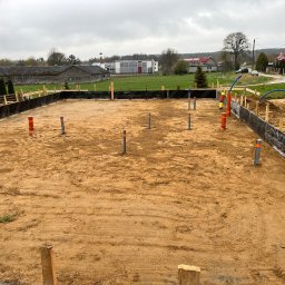 Michał Wieczorek DOMY DREWNIANE ,SZKIELETOWE. OBSŁUGA KOMPLEKSOWA - Przygotowany teren pod budowę domu z widocznym szalunkiem, wystającymi rurami kanalizacyjnymi i przyłączami, w tle zabudowa wiejska.