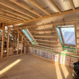 Poddasze w trakcie ocieplania, widoczne okna dachowe, folia aluminiowa izolacyjna na skosach, drewniana konstrukcja szkieletowa, częściowo ocieplona ściana z widocznymi membranami Siga Majrex...