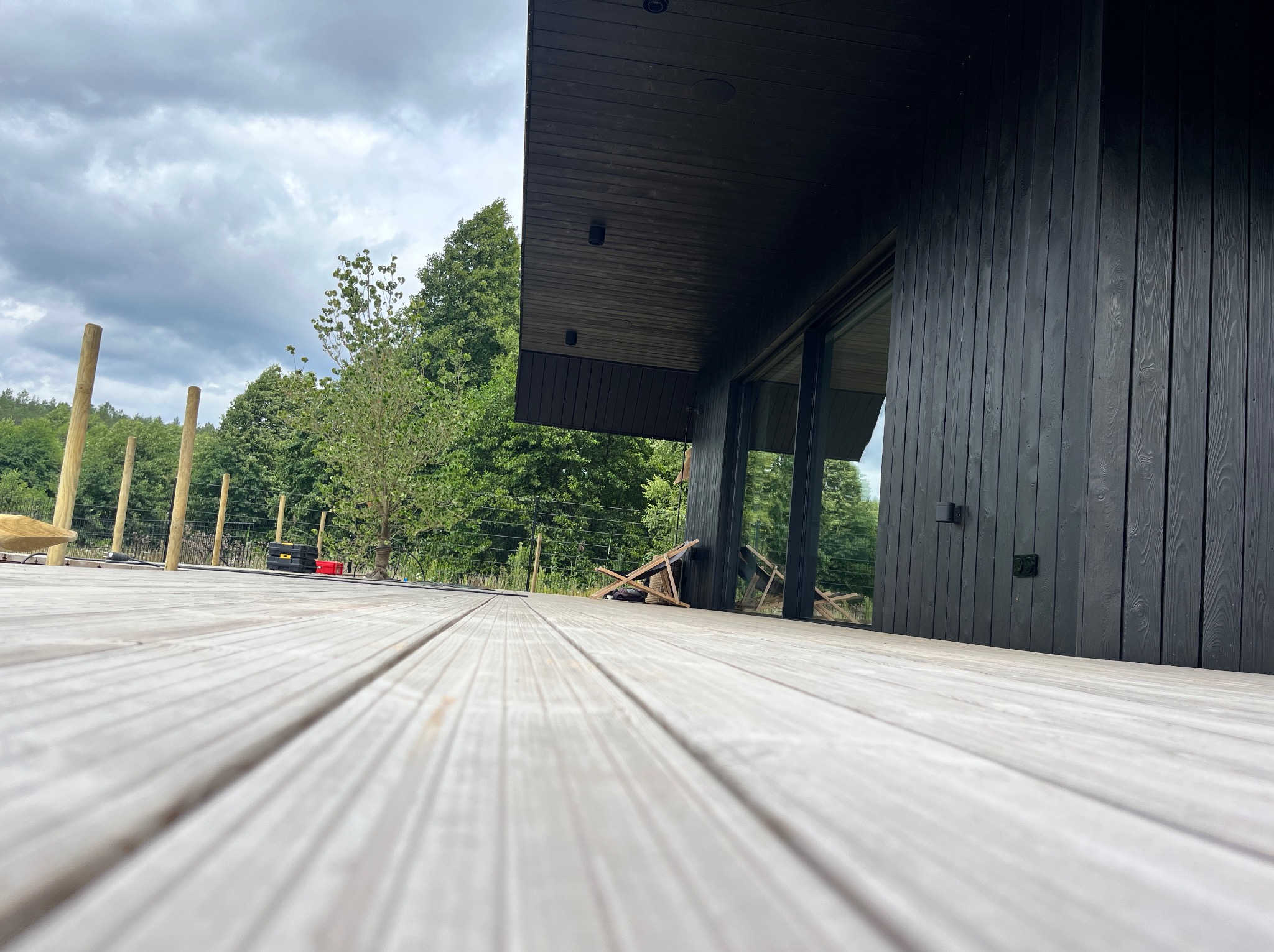 Nowoczesny dom z ciemną drewnianą elewacją widziany z niskiej perspektywy z drewnianego tarasu, z widocznymi narzędziami i elementami budowy.