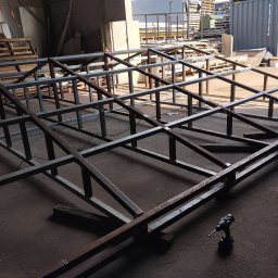 PAZ-MET PRZEMYSŁAW PAZIO - Konstrukcja szkieletowa z metalowych profili w hali produkcyjnej, widoczna wiertarka akumulatorowa, poziomica i fragmenty materiałów.