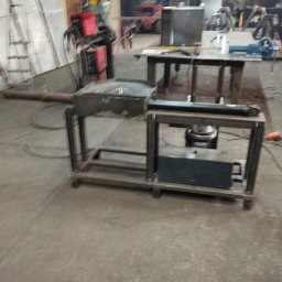 PAZ-MET PRZEMYSŁAW PAZIO - Warsztatowa sceneria z metalowym stołem roboczym, spawarką i wózkiem widłowym w tle, ukazująca środowisko pracy ślusarza lub spawacza.