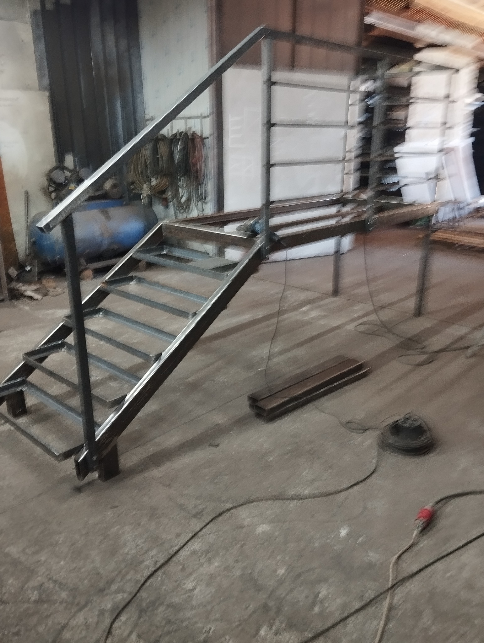 Konstrukcja schodów i podestu z metalowych profili w warsztacie, widoczne narzędzia i materiały spawalnicze w tle.