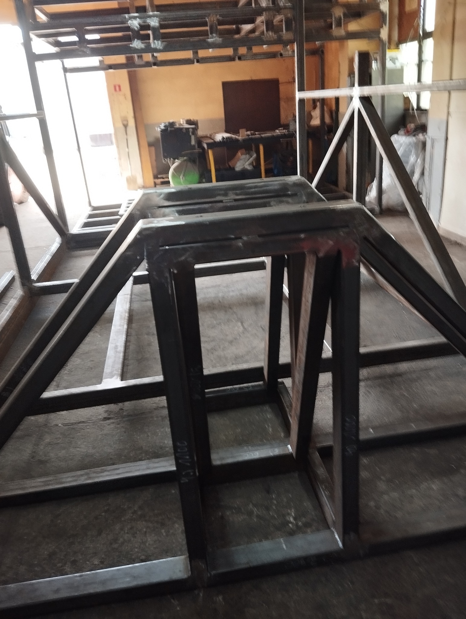 Konstrukcja metalowa z profili, prawdopodobnie szkielet pod budowę, widoczne spawy i oznaczenia na metalu, warsztatowe tło.