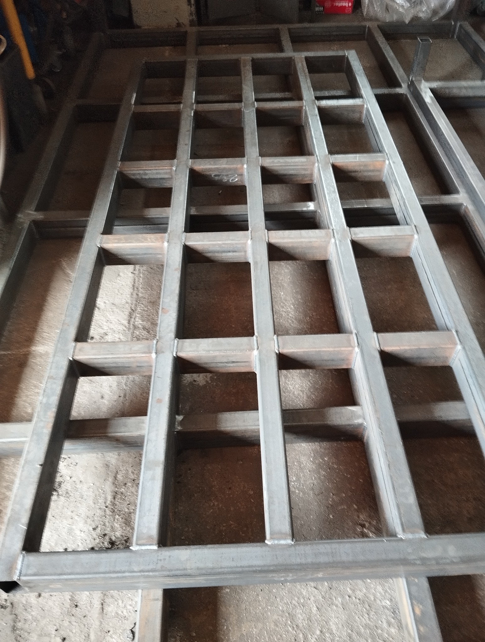 Konstrukcja z profili stalowych spawanych w kratownicę, leżąca na betonowej posadzce, widoczne spawy.