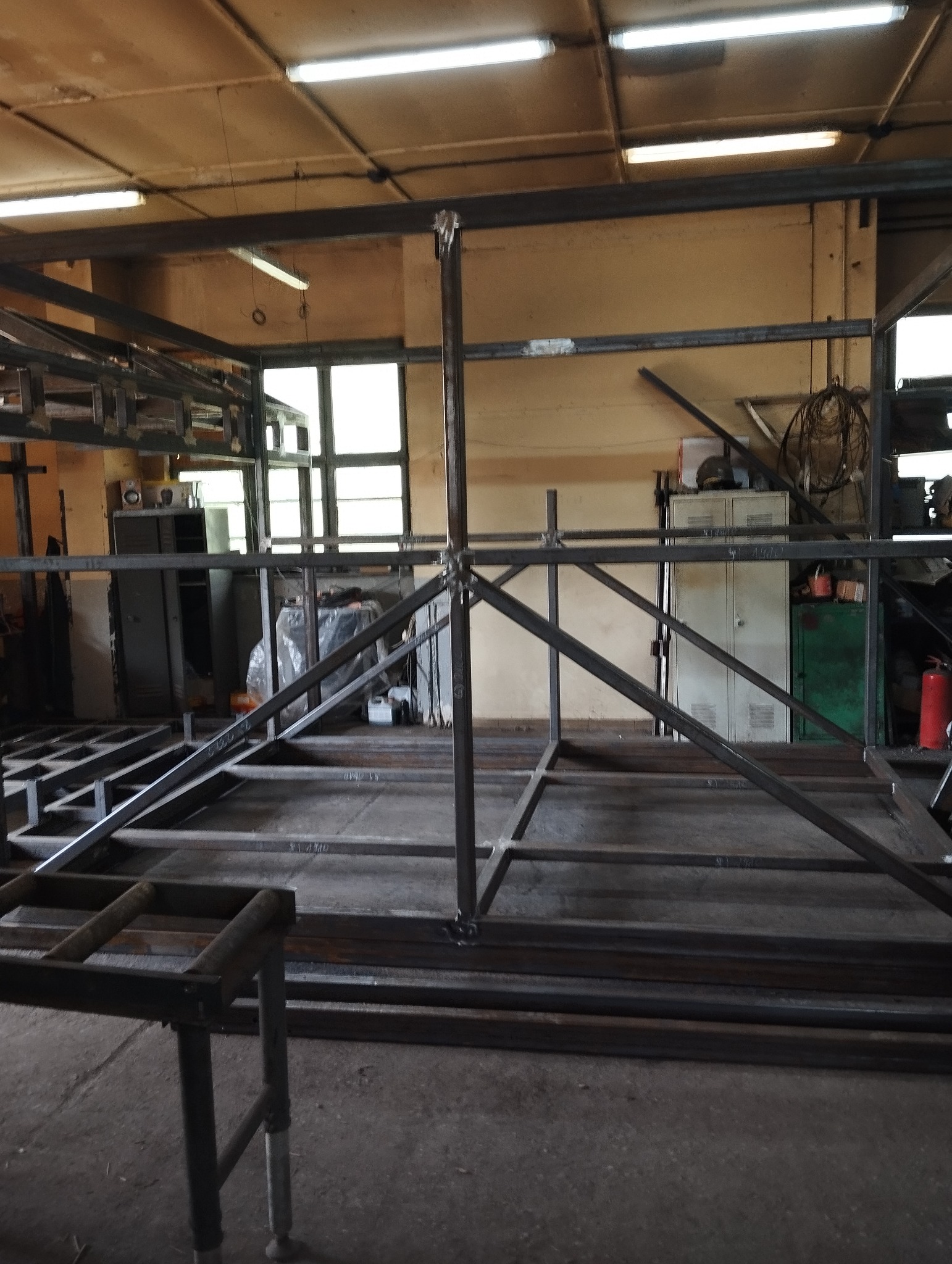 Konstrukcja metalowa spawana w warsztacie, widoczne spawy, profile stalowe tworzące szkielet, w tle okna i wyposażenie warsztatu.