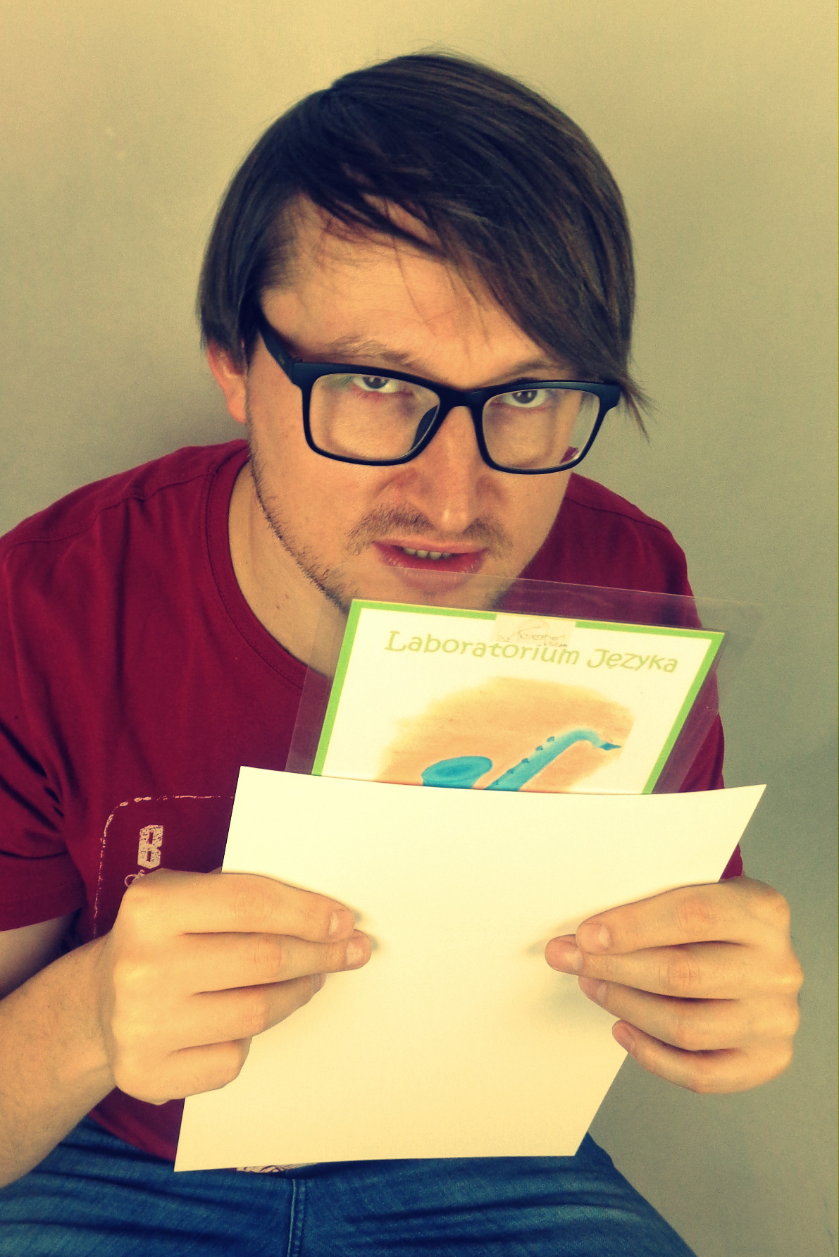 Mężczyzna w okularach trzyma kartkę z napisem 'Laboratorium Języka' i czystą kartkę.