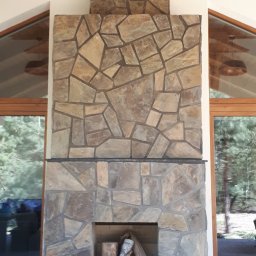 Kominek z otwartym paleniskiem na zadaszonym tarasie obłożony naturalnym kamieniem