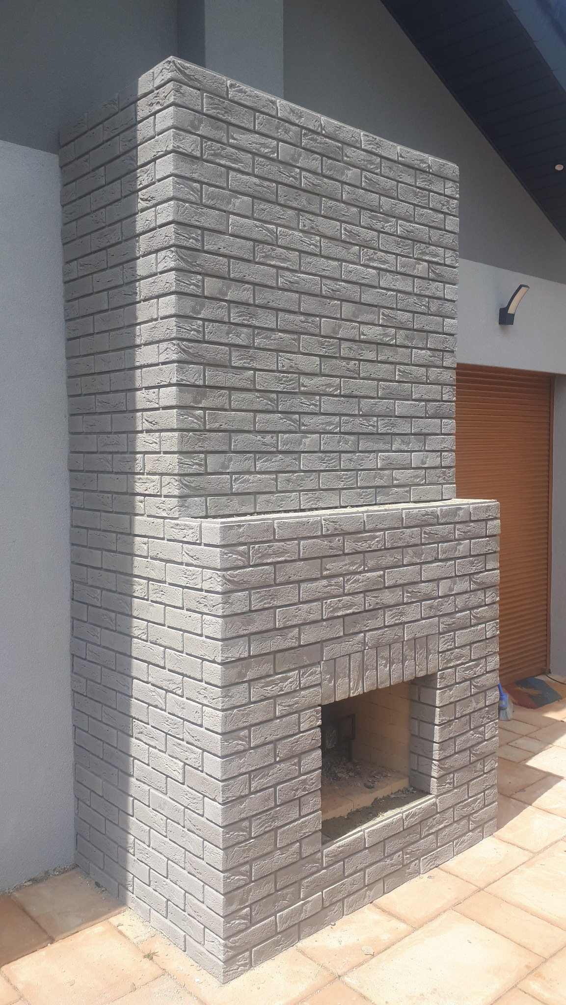 Kominek z otwartym paleniskiem na tarasie oklejony cegiełką elewacyjną