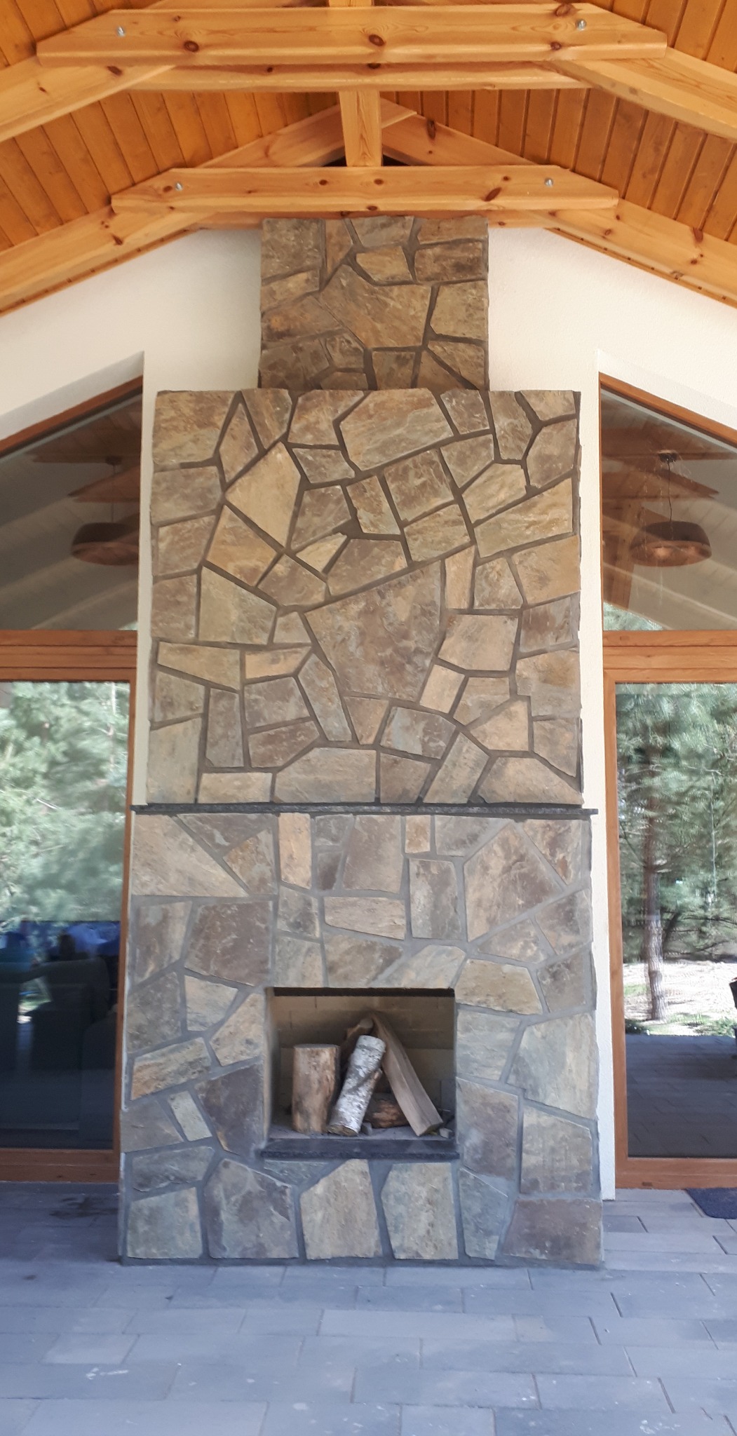 Kominek z otwartym paleniskiem na zadaszonym tarasie obłożony naturalnym kamieniem
