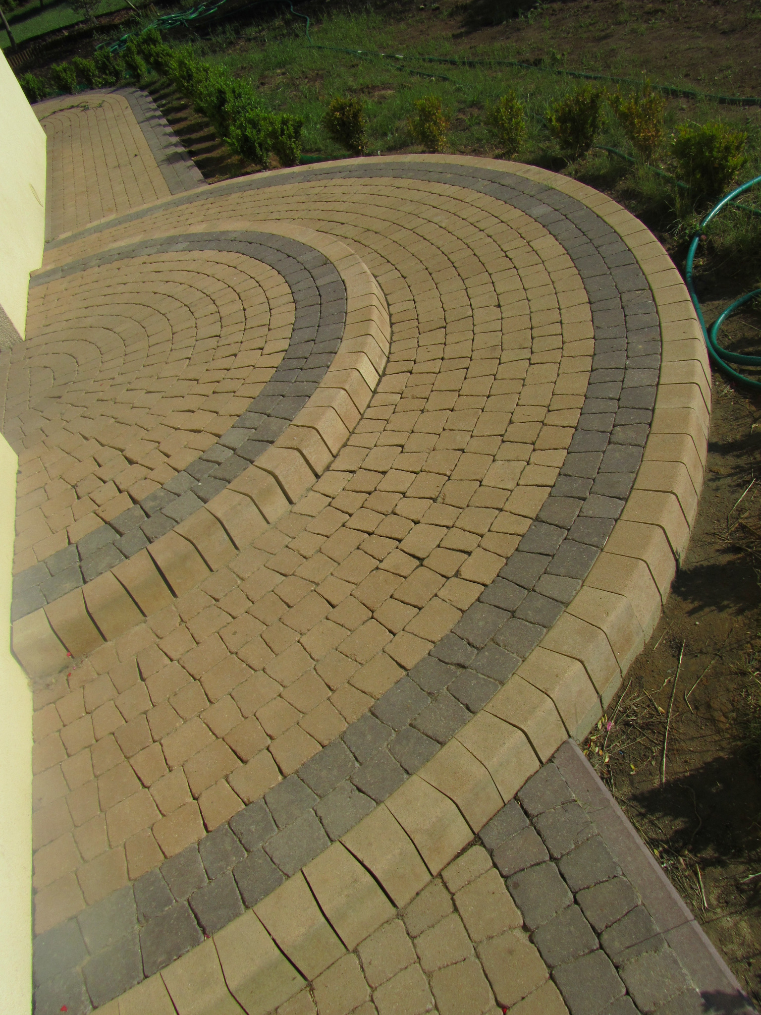 Ułożona nawierzchnia z dwukolorowej kostki brukowej tworząca półokrągły wzór z obrzeżem, widok z góry.