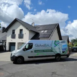 Srebrny van firmy GlobalBAU zaparkowany na ulicy przed domem z panelami słonecznymi na dachu, błękitne niebo z chmurami w tle.