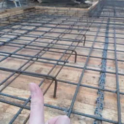 Zbrojenie fundamentu ułożone na deskowaniu z widocznym elementem dystansowym i kciukiem dającym perspektywę skali.