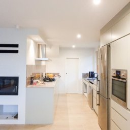 MONTOWNIA DOMÓW SPÓŁKA Z OGRANICZONĄ ODPOWIEDZIALNOŚCIĄ - Wnętrze domu w trakcie wykańczania: widoczny kominek z czarnym wkładem, jasna kuchnia z zabudową meblową, okno z drewnianą ramą i widok na zewnątrz, częściowo wykończona podłoga i czerwona gaśnica...