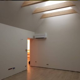 MONTOWNIA DOMÓW SPÓŁKA Z OGRANICZONĄ ODPOWIEDZIALNOŚCIĄ - Poddasze po remoncie: świeżo pomalowane ściany w odcieniach bieli, drewniane belki stropowe, klimatyzator na ścianie, widoczne punkty elektryczne i jasna podłoga z paneli.