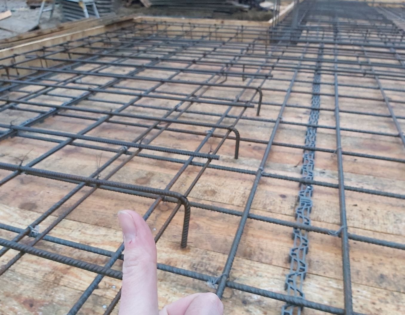 Zbrojenie fundamentu ułożone na deskowaniu z widocznym elementem dystansowym i kciukiem dającym perspektywę skali.