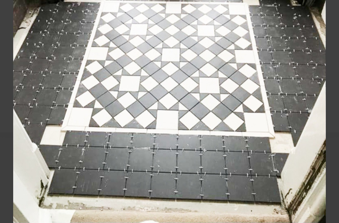 Podłoga w trakcie układania płytek w czarno-białą szachownicę. Część płytek już ułożona, część jeszcze nie, widoczne krzyżyki dystansowe.